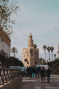 People walking on street amidst buildings in city against sky