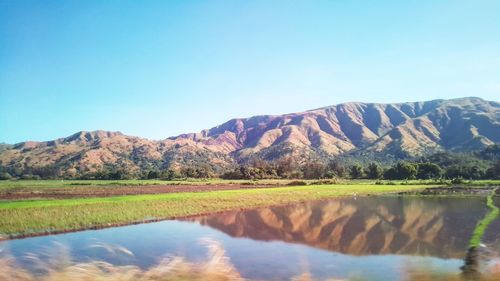 Scenic view of lake and mountains against clear blue sky