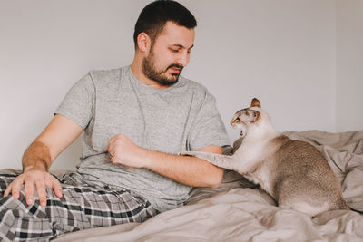 Man sitting with cat on bed at home