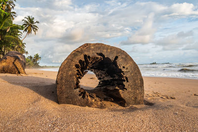 Old rusty wheel on beach against sky