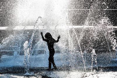 Silhouette girl enjoying amidst fountain at park