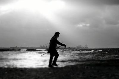 Silhouette man walking at beach against cloudy sky