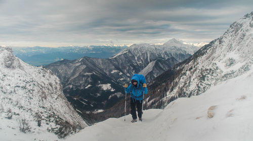 Woman hiking uphill on snowcapped mountain against sky