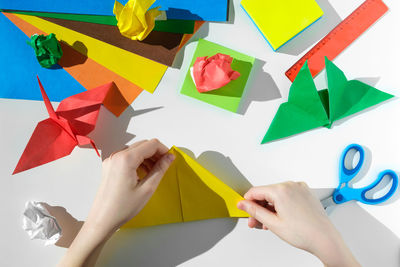 Paper crafts, scissors, colored paper sheets, scraps, on white table. origami. preschooler. top view