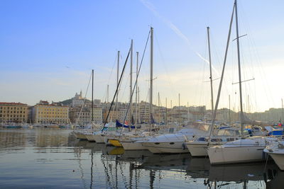 Sailboats moored in harbor at sunset