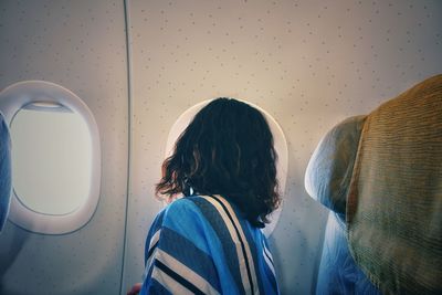 Side view of woman looking through window while traveling in airplane