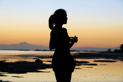 Silhouette woman photographing sea against sky during sunset