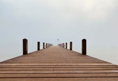 Wooden jetty leading to sea against clear sky