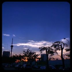 Silhouette trees by street against blue sky