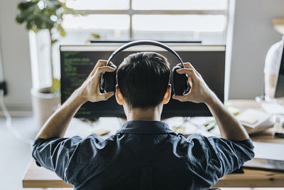 Rear view of male programmer wearing headphones in office