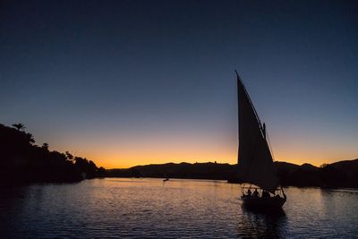 Silhouette sailboat sailing on sea against clear blue sky during sunset