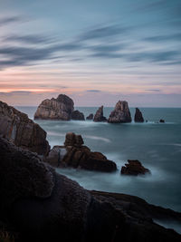 Rocks in sea against sky during sunset