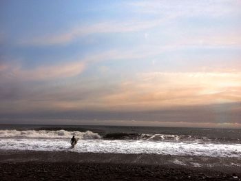 Person wading in sea against sky during sunset