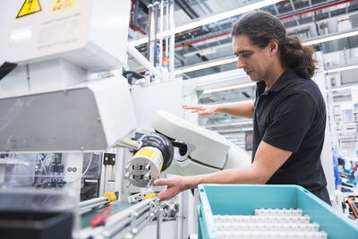 Man operating assembly robot in factory