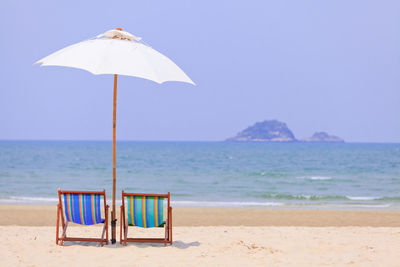 Deck chairs on beach against sky