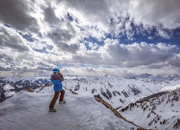 Side view of man standing on snowcapped mountains against cloudy sky