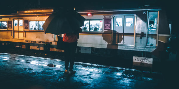 Rear view of woman holding umbrella while standing at railroad station