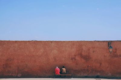 Rear view of men on wall against clear blue sky