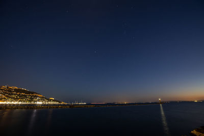 Illuminated city by sea against sky at night