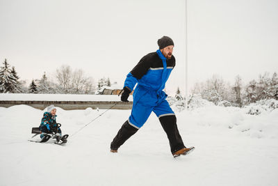 Fun dad pulling sleigh where son is sitting on in winter snowy woods