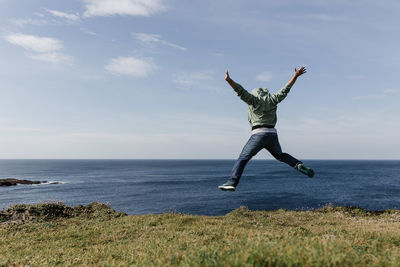 Man jumping on grassy field by sea against sky