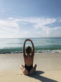 Rear view of woman holding sunglasses at beach against sky