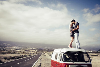 Couple embracing on van by road against sky