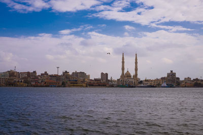 City at waterfront against cloudy sky