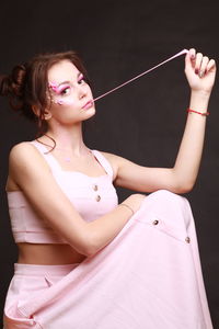 Beautiful young woman with make-up stretching bubble gum against gray background