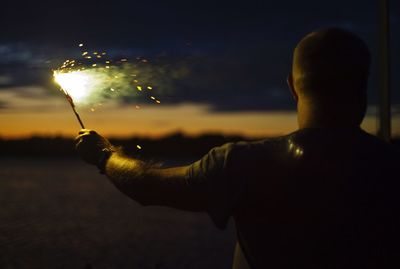 Rear view of man holding sparkler on field at night