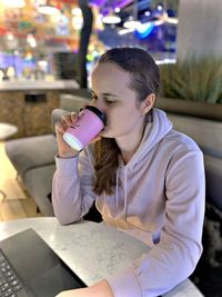 Young woman drinking water while sitting on table