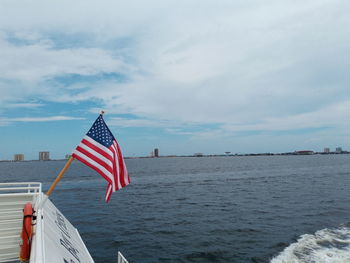 Flag on red boat in sea against sky