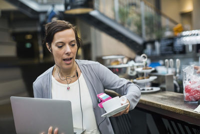 Panic mature woman holding laptop and coffee at cafe