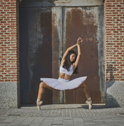Ballerina sitting on seat against brick wall