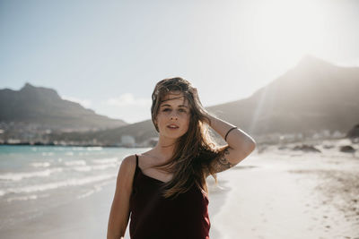 Portrait of young woman standing on beach against sky