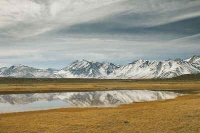 Scenic view of landscape by snowcapped mountains against cloudy sky