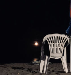 Empty chairs and table at beach against sky at night