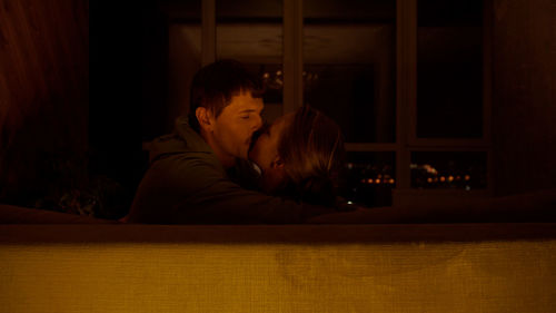 Couple kissing by window at night