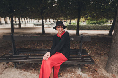 Full length portrait of woman sitting on bench in park