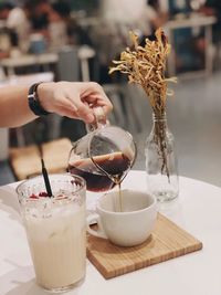 Close-up of hand pouring drink in glass on table