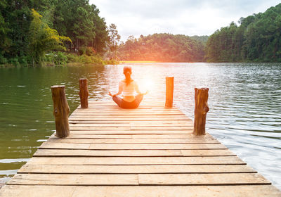 Rear view of woman relaxing on pier over lake against sky