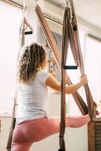 A girl with curly hair practices yoga with a hammock. yoga, aero yoga, fitness, lifestyle. rear view