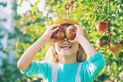 Smiling girl covering eyes with apples