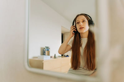 Beautiful teenage girl in headphones singing at the mirror at home