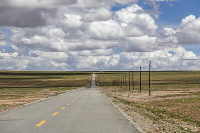 Under the blue sky and white clouds, a straight, flat, unmanned asphalt road leads to the horizon