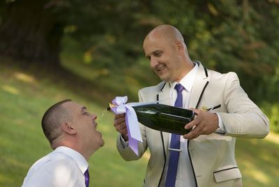 Groom pouring alcohol in friend mouth during wedding celebration