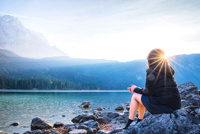 Woman sitting on rock by lake against mountains