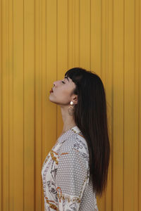 Woman looking away while standing against yellow wall