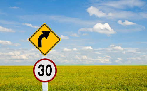 Road sign on field against sky