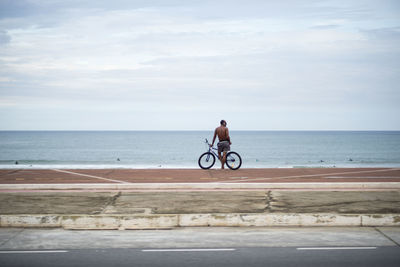 Man riding bicycle by sea against sky